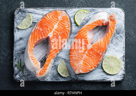 Zwei rohe frische Lachs oder Forelle Steaks, reich an Omega-3 Öl, mit Kalk, Thymian und Olivenöl auf einem dunklen Hintergrund. Gesunde und diätetische Lebensmittel. Ansicht von oben. Fl Stockfoto