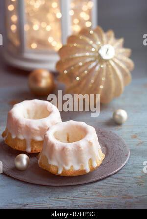 Close-up auf bundt Kuchen am grünen Tisch im Landhausstil mit Weihnachtsbeleuchtung in Weiß Laterne und funkelnde goldene Schmuckstück Stockfoto