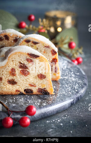 Christstollen auf dunklen festlichen Hintergrund mit Kerze, Beeren und Blätter. Traditionelle deutsche Dessert für Weihnachten feiern. Stockfoto