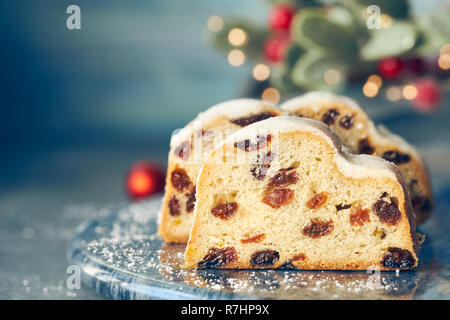 Christstollen auf blau-grünen Hintergrund mit festlichen Weihnachtsbeleuchtung und roten Beeren im Winter. Traditionelle deutsche Dessert für Weihnachten feiern. Stockfoto