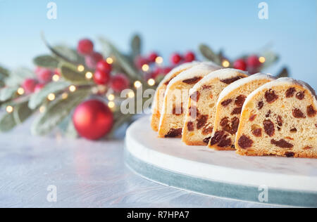 Christstollen auf Weiß-Blau festliche Hintergrund mit Beeren und Weihnachtsbeleuchtung. Traditionelle deutsche Dessert für Weihnachten feiern. Stockfoto
