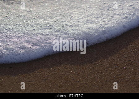 Makro Foto von Meer Wasser Schaum an einem Sandstrand in der Morgensonne. Aberdeen, Schottland, Großbritannien. Stockfoto