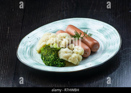 Brokkoli, Blumenkohl, Wurst, in eine weiße Platte auf einem dunklen Hintergrund. Frühstück, gesunde Lebensmittel Stockfoto