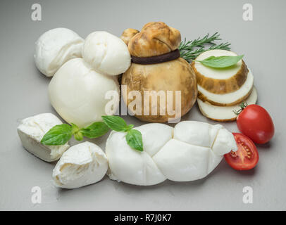 Mozzarella und Scamorza, traditionelle italienische Käse mit frischen Kräutern auf grauem Hintergrund. Stockfoto