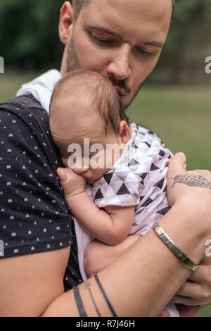 Pflege junger Vater außerhalb schaukelnd seine adorable Baby Boy Stockfoto