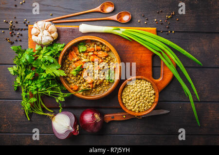 Linsen vegane Suppe in eine hölzerne Schüssel und Zutaten auf einem weißen Holz- Hintergrund, Ansicht von oben. Stockfoto
