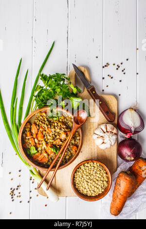 Linsen vegane Suppe in eine hölzerne Schüssel und Zutaten auf einem weißen Holz- Hintergrund, Ansicht von oben. Stockfoto