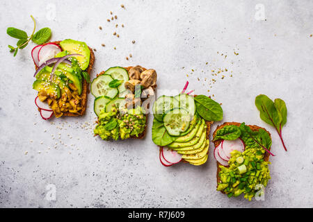 Avocado Toast mit verschiedenen Belägen, Ansicht von oben, weisser Hintergrund. Auf Basis pflanzlicher Ernährung Konzept. Stockfoto