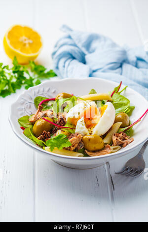 Thunfisch Salat mit Nudeln, Oliven und pochiertem Ei in eine weiße Platte auf einem weißen Holz- Hintergrund. Stockfoto