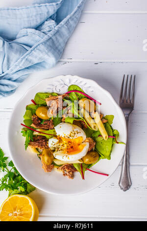 Thunfisch Salat mit Nudeln, Oliven und pochiertem Ei in eine weiße Platte auf einem weißen Holz- Hintergrund. Stockfoto