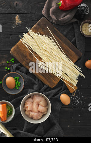 Ansicht von oben Zutaten zum Kochen udon Nudeln mit Hühnerfleisch auf dunklen Holztisch in der Küche zu Hause Stockfoto