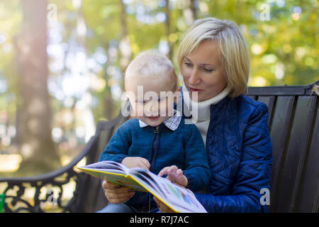 Mamma zu einem Kind liest ein Buch im Park spazieren. Ein Buch mit einem Kind Stockfoto