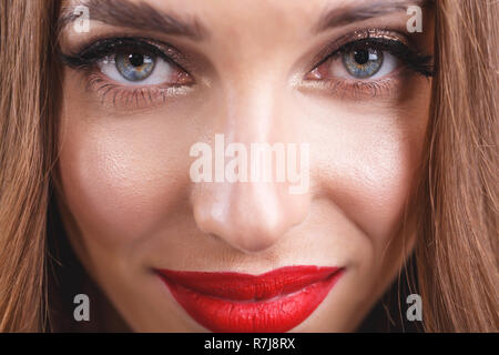 7/8-Ansicht von attraktiven Romantische langhaarige Frau mit roten Lippen mit schwarzen Kleid steht auf dem grauen Hintergrund Stockfoto