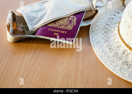 Reiseanliegen Konzept für Auslandsreisen Britischer biometrischer Reisepass in einer Brieftasche mit Sonnenhut für Frauen auf einer Tischplatte. England, Großbritannien Stockfoto