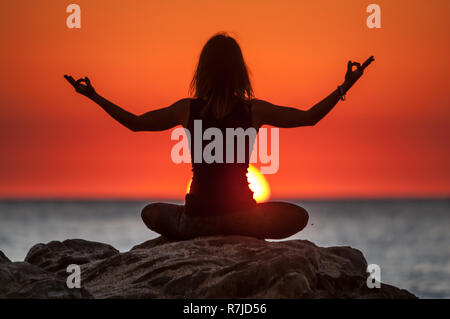 Argelès-sur-Mer (Frankreich). Jemand Yoga auf den Felsen vor der Racou Strand bei Sonnenaufgang. Schöne junge Frau mit braunen Stockfoto