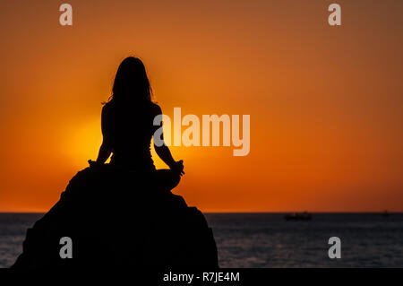 Argelès-sur-Mer (Frankreich). Jemand Yoga auf den Felsen vor der Racou Strand bei Sonnenaufgang. Schöne junge Frau mit braunen Stockfoto