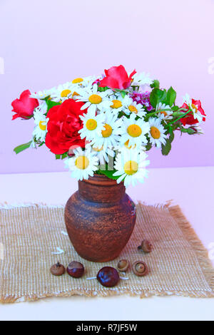 Blumenstrauß aus den weißen Gänseblümchen und rote Rosen in Lehmtöpfen ist auf Entlassung. Blumen im Topf auf lila Hintergrund. Gänseblümchen und rote Rosen in der Vase auf dem Tisch Stockfoto