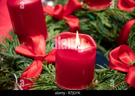 Rote brennende Kerze auf dem Adventskranz mit grünen Zweigen Stockfoto