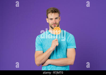 Geschmack der Kindheit. Mann schöner macho Essen großen bunten süßen Lutscher. Mann mit Borsten mag Lollipop. Cheat meal Konzept. Zucker schädlich für die Gesundheit. Kerl halten Lollipop candy violett unterlegt. Stockfoto