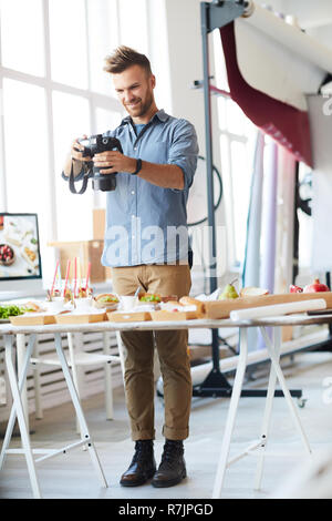 Volle Länge Portrait von lächelnden Fotograf Bilder von Partei, während im Studio arbeiten Stockfoto