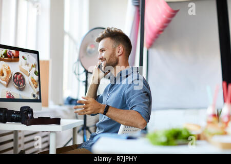 Seitenansicht Portrait von stattlichen Fotograf sprechen telefonisch beim Sitzen am Schreibtisch im Studio, Kopie Raum Stockfoto