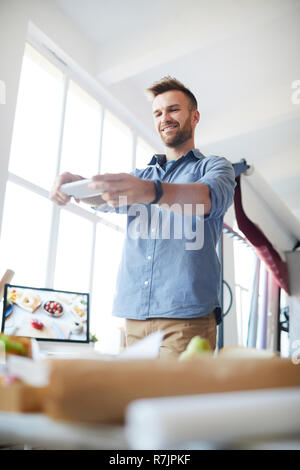 Low Angle Portrait von gutaussehenden jungen Mann fotografieren Sie ihr Smartphone in Photo Studio Stockfoto