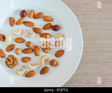 Nüsse, Mandeln, Haselnüsse, Walnüsse, Cashewnüsse auf weiße Platte auf einem Holztisch. Gesunde organische Snacks, Frühstück, Food Ingredients. Flach Top-Down Stockfoto
