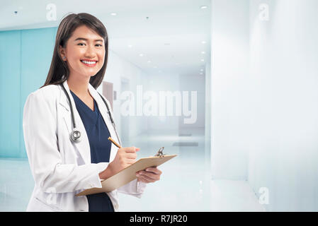 Lächelnd asiatischen Arzt Frau tragen Laborkittel Notizen in der Zwischenablage in Klinik Stockfoto