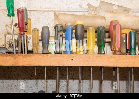 Alte Sandpapier und Schraubendreher gespeichert aufrecht in Bohrungen in ein Holz Regal in einem Workshop gebohrt Stockfoto