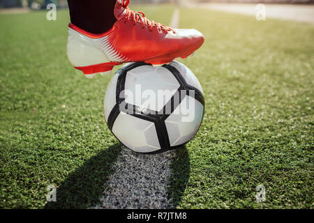 Nahaufnahme von Fußballspieler Füße in socker Turnschuhe. Er hält ihn auf die Kugel. Kugel stehen auf weißen Linie auf Rasen gemalt. Stockfoto
