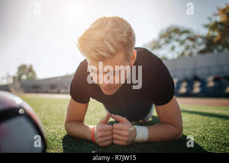 Blonde junge Spieler stehen in Ganzkörperstütz auf Fußball-Rasen. Er ist konzentriert. Ball lag neben ihm. Guy ist allein. Stockfoto