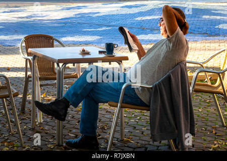 Mann in einem teeshirt ein Taschenbuch zu einem Outside cafe Tabelle in der Alameda de Hercules in Sevilla, Spanien lesen Stockfoto
