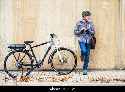 Active Senior Mann mit electrobike stehen draußen in der Stadt, mittels Smartphone. Stockfoto