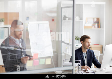 Porträt von zwei modernen Menschen arbeiten im Büro in Kabinen durch Glaswände getrennt, cop Platz Stockfoto