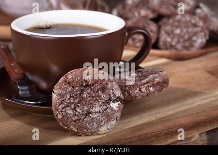 Nahaufnahme des chocolate fudge Cookie und Tasse Kaffee mit Platte von Cookies im Hintergrund Stockfoto
