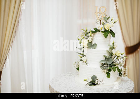 Weisse Hochzeitstorte mit Blumen. Das Wort Liebe mit Herz. Stockfoto