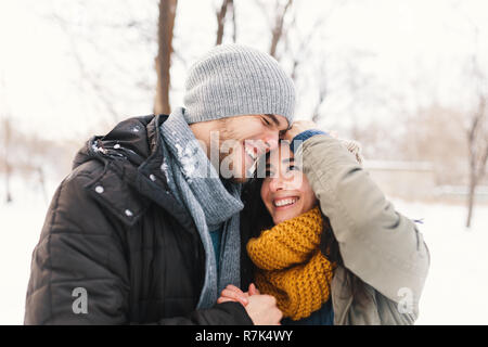 Glückliches junges Paar beim Winterurlaub lachend und Umarmen auf einer unscharfen Winter Landschaft Hintergrund. Stockfoto