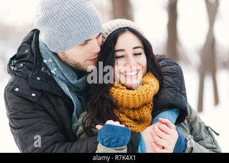 Glückliches junges Paar beim Winterurlaub Lächeln und Umarmungen auf einer unscharfen Winter Landschaft Hintergrund. Stockfoto