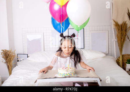 Kleine asiatische Mädchen bläst die Kerzen auf Kuchen und einen Wunsch. Stockfoto