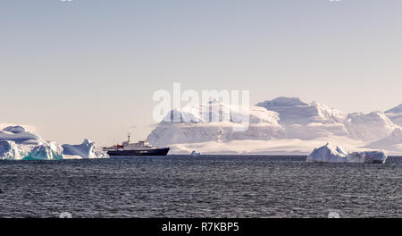 Touristischen Kreuzfahrtschiff unter blauen Eisberge in der Nähe von Cuverville Insel, Antarktis Stockfoto