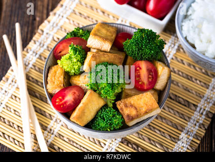 Gegrillter Tofu mit Brokkoli und Tomaten in Weiß Schüssel auf Bambus Pad mit Stäbchen auf der linken Seite. Stockfoto