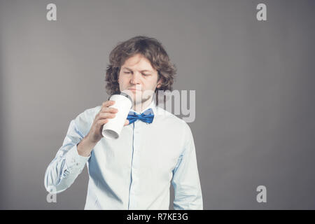 Close up Portrait von glücklich aussehenden Mann im blauen Hemd mit Papier Tasse Kaffee am Morgen. Guten Morgen mit Kaffee. Takeaway Kaffee, Zeit für die Kaffeepause. Kerl wird Kaffee aus Einweg Kelch zu trinken, Stockfoto