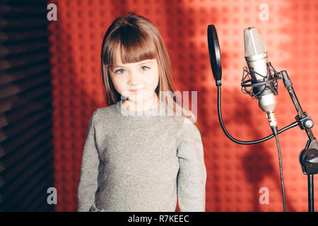 Wunderschöne kleine Mädchen mit Mikrofon auf rotem Hintergrund Stockfoto