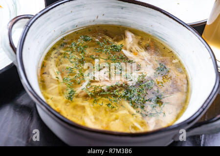 Schüssel Hühnerbrühe. Hühnersuppe in eine weiße Platte auf einem schwarzen Holztisch. Freier Platz für Text. Blick von oben. Ansicht von oben. Stockfoto