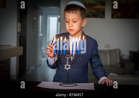 Cute Kaukasischen jüdischer Junge Beleuchtung Kerzen auf einem traditionellen Hanukkah Menorah Armleuchter, jüdischen Feiertagen Konzept. Stockfoto