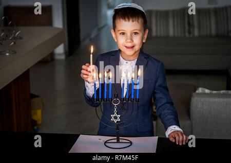 Cute Kaukasischen jüdischer Junge Beleuchtung Kerzen auf einem traditionellen Hanukkah Menorah Armleuchter, jüdischen Feiertagen Konzept. Stockfoto