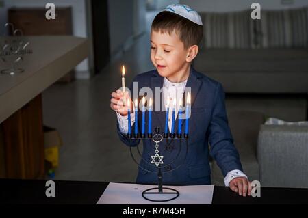 Cute Kaukasischen jüdischer Junge Beleuchtung Kerzen auf einem traditionellen Hanukkah Menorah Armleuchter, jüdischen Feiertagen Konzept. Stockfoto