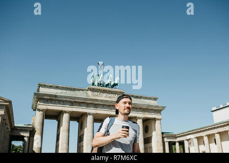 Eine Person, die Getränke aus einer Tasse Kaffee oder einem anderen Getränk bei einem Spaziergang oder beim Sightseeing in Berlin in Deutschland. Die Zukunft ist das Brandenburger Tor. Stockfoto