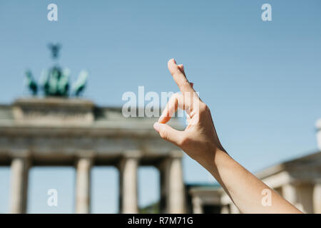 Eine Person zeigt ein Zeichen mit seinen Fingern, dass bedeutet, alles vor dem Hintergrund des Brandenburger Tor und blurry unkenntlich Menschen in Berlin in Deutschland gut ist. Stockfoto