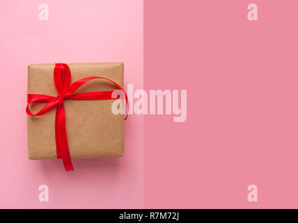 Geschenkbox in braun gefärbte Handwerk Papier gewickelt und mit roter Schleife auf rosa Hintergrund mit Copyspace gebunden. Stockfoto